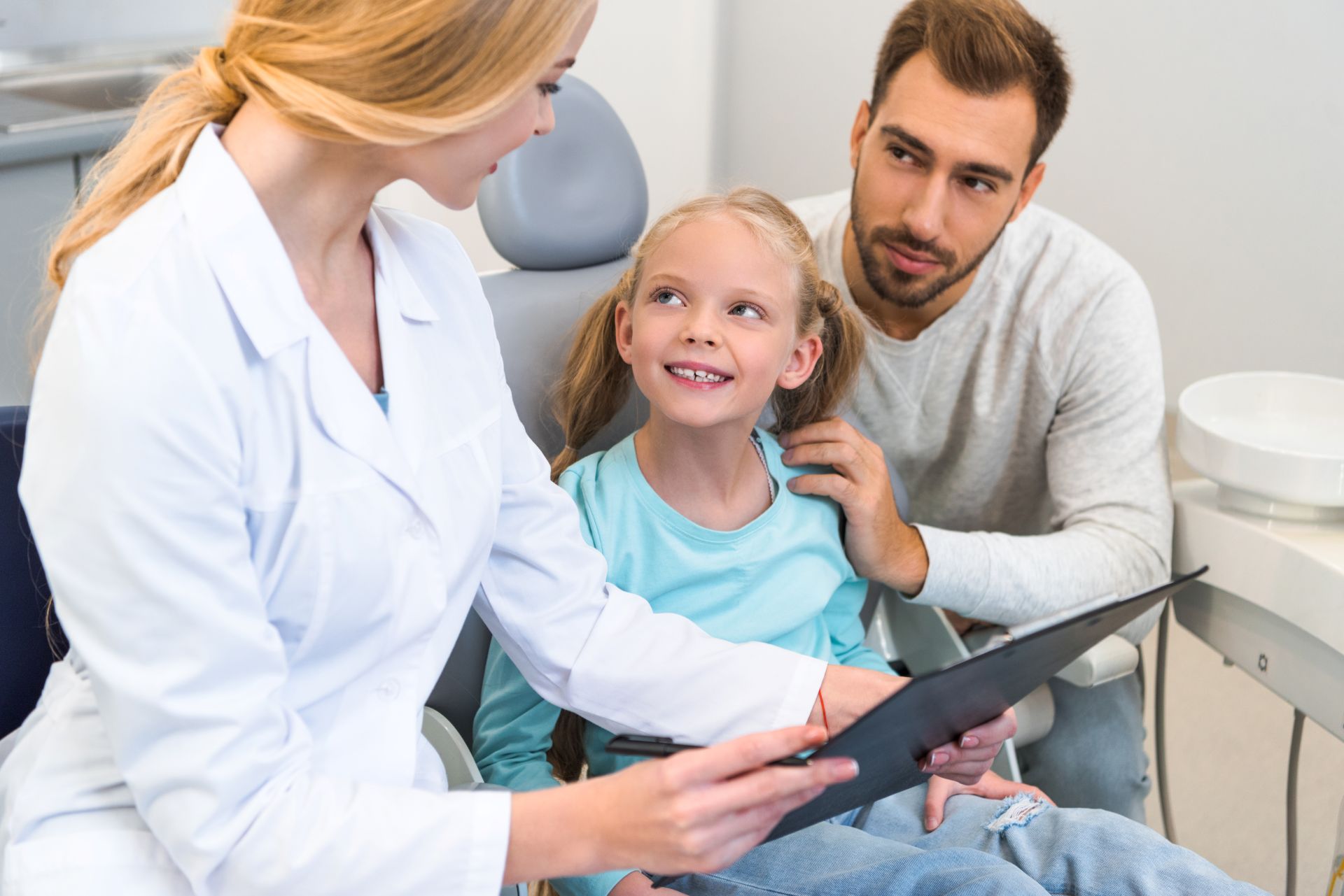 A young girl and her father talking with a dentist during a dental visit