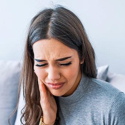 Young woman clutching side of face from jaw pain