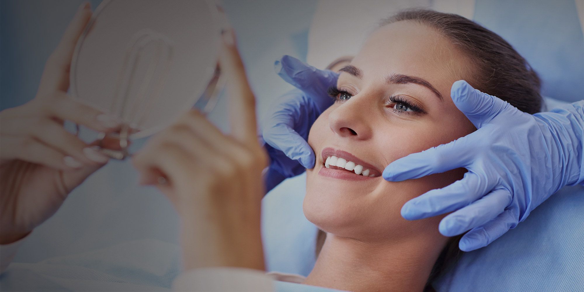 Woman looking at her smile in the mirror while the dentist's gloved hands hold her head