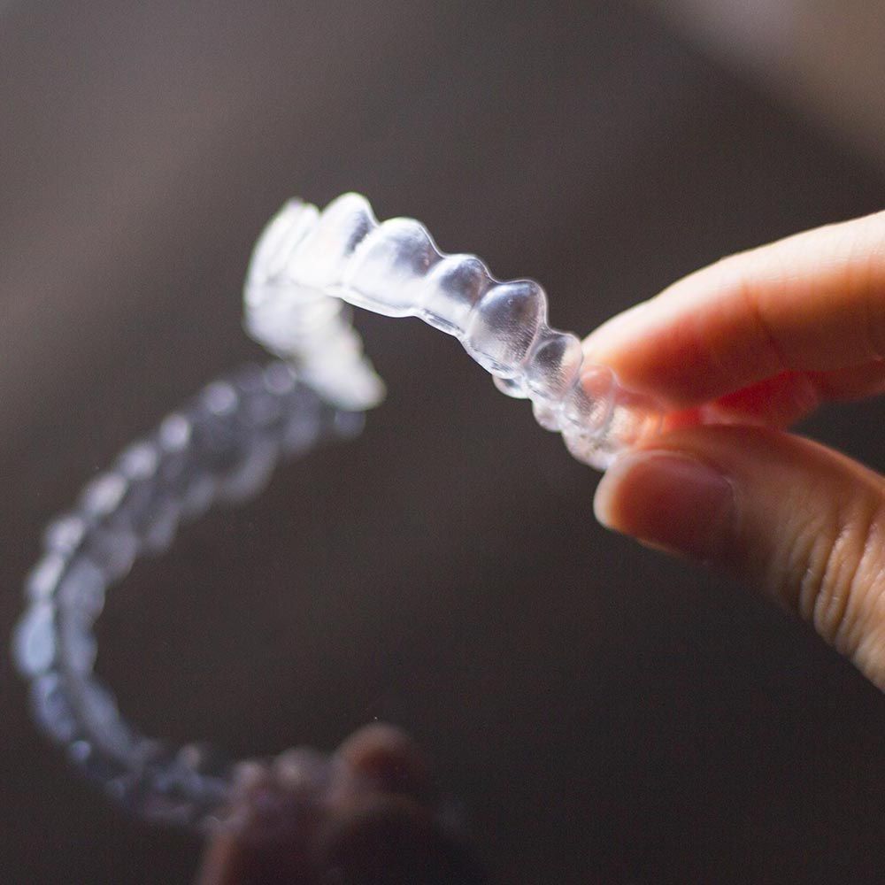Person holding clear aligner against a dark background